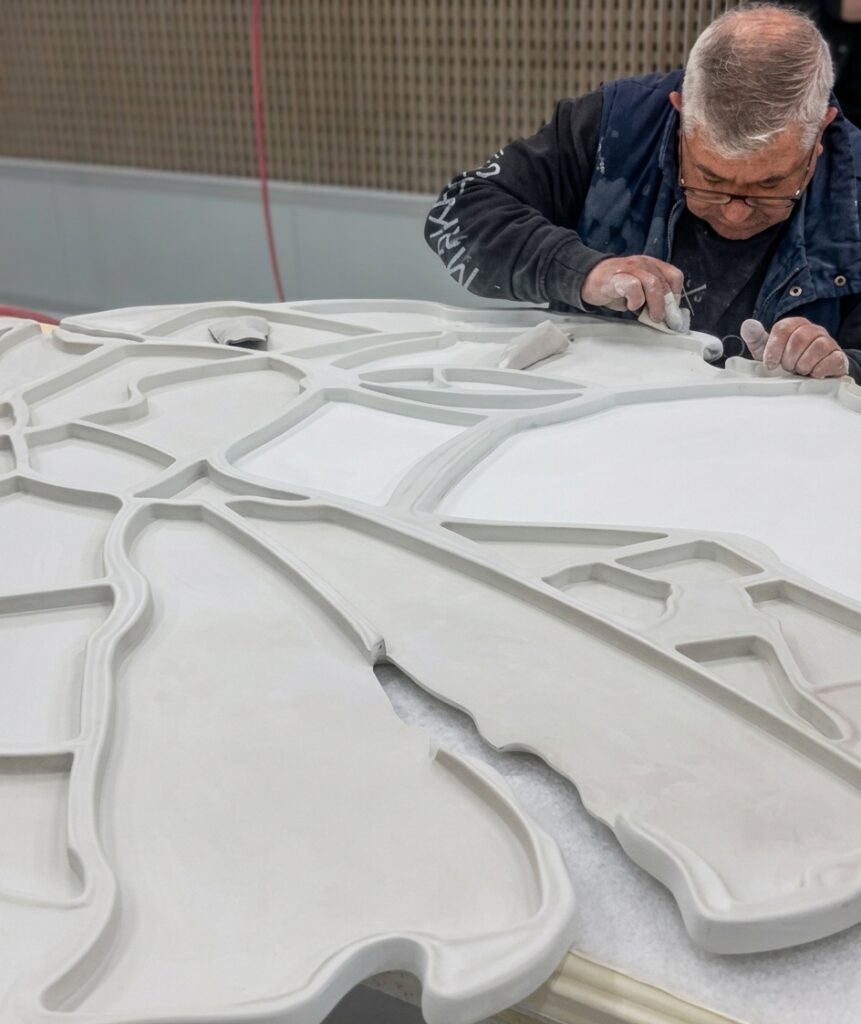 Artisan ponçant à la main un grand panneau décoratif sur mesure dans un atelier de fabrication