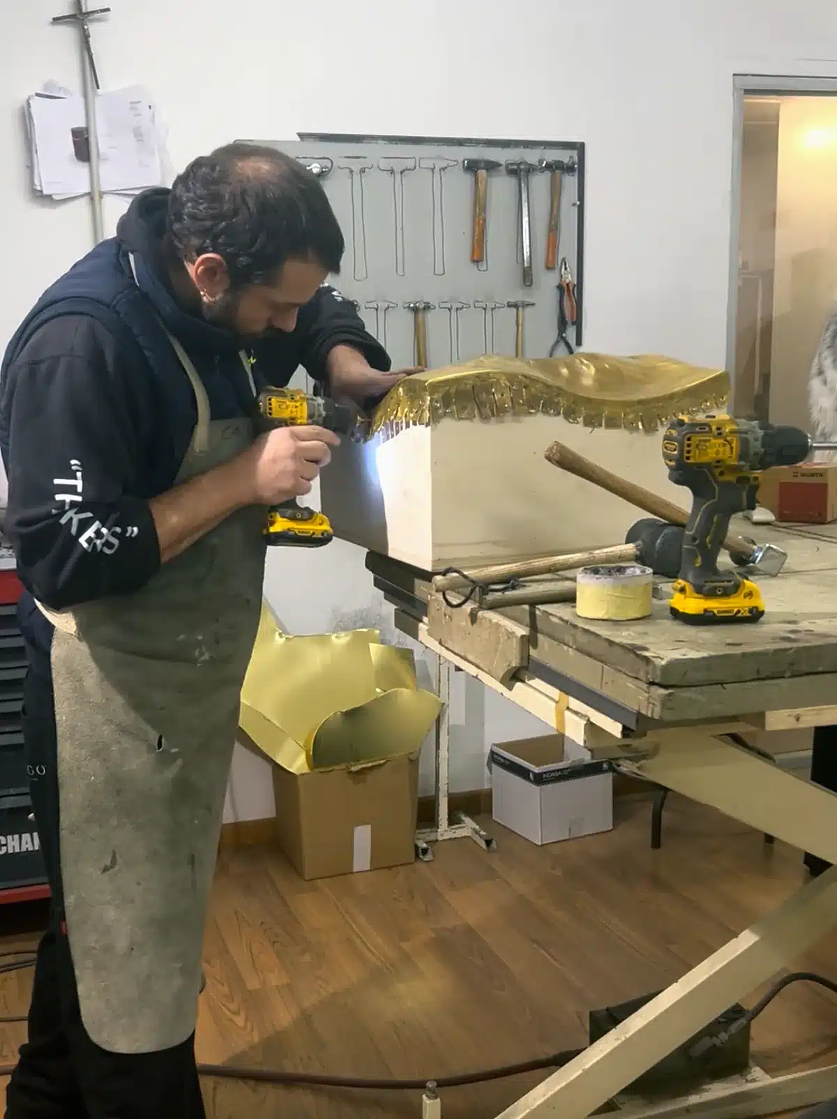Artisan façonnant un placage métal doré sur un meuble sur mesure, atelier partenaire région de Porto